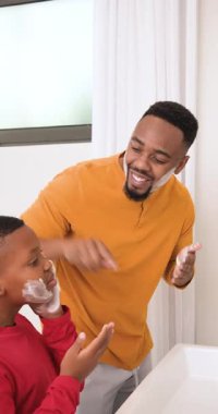 Dikey video: Afro-Amerikan baba köpük dağıtıyor, oğul lavaboda tıraş taklidi yapıyor. Aile, bakım, bağlanma, akıl hocalığı, cilt bakımı, gelenek, dikey video