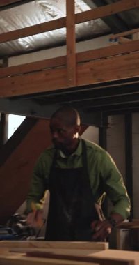 Dikey video: Afro-Amerikan marangoz dükkanında kare işaretli ahşap alıyor, çerçeveyi birleştiriyor. Atölye, işçilik, ahşap işçiliği, işbirliği, hassasiyet, inşaat, dikey video