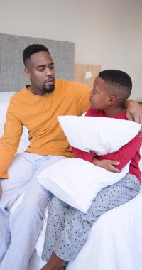 Dikey video: Afrikalı Amerikalı baba ve oğul teselli ediyor, yatakta yastık kavgası yapıyor kahkahaları paylaşıyor. Aile, yakınlaşma, şefkat, neşe, sıcaklık, boş zaman, dikey video