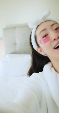 Dikey video: Çinli bir kadın, yatak odasında pembe yamaları cilt bakımı için düzeltiyor. Güzellik, cilt bakımı, özgüven, rahatlama, minimalizm, dikey video