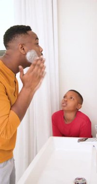 Dikey video: Afrikalı Amerikalı baba oğluyla konuşuyor, krem sürüyor, lavaboda jilet kullanmayı öğretiyor. Babalık, akıl hocalığı, tımar, eğitim, yerli, cilt bakımı, dikey video