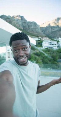 Dikey video: Afro-Amerikalı adam telefonu kaldırıyor, kaydediyor, terastaki dağ manzarasını işaret ediyor. Açık hava, modern, yaşam tarzı, doğa, manzara, iletişim, dikey video