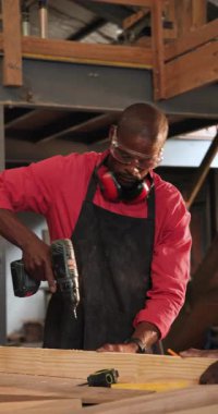 Dikey video: Afrikalı Amerikalı adam bant işaretlerini takip ediyor, tezgahta delik açıyor. Sanatçılık, marangozluk, endüstriyel, zanaatkar, kılavuz, atölye, dikey video