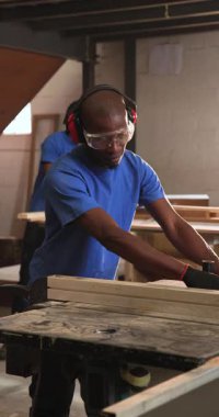 Dikey video: Afrikalı Amerikalı erkek marangoz beslenme kurulu atölyede doğruluğu kontrol ediyor. Zanaatkar, atölye, marangozluk, aletler, değirmen, dikey video
