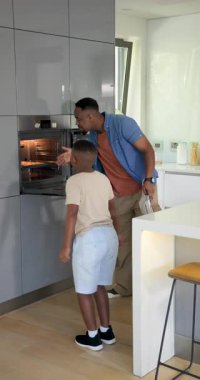 Dikey video: Afrika kökenli Amerikalı baba ve oğul fırından pizza tepsisini çıkarıyorlar. Aile, aşçılık, modern, yaşam tarzı, bağlanma, ev, dikey video