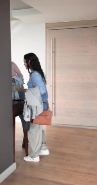 Dikey video: Kadın arkadaşlar bardaklarla salona giriyor, onları yerleştiriyor ve tablet yönlerini kontrol ediyorlar. Arkadaşlık, güncel, çağdaş, yaşam tarzı, ev, iletişim, dikey video