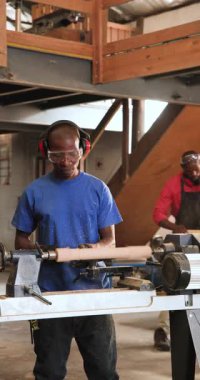 Dikey video: Afrikalı Amerikalı iş arkadaşları dükkânda ölçüm tahtası ve danışmanlık yapıyor, silindiri şekillendiriyor. Sanatçılık, atölye, kesinlik, işbirliği, sanayi, zanaat, dikey video