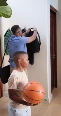 Vertical video: African American father and son entering foyer tossing orange basketball for catch. Family, bonding, home, activity, outdoor, casual, vertical video