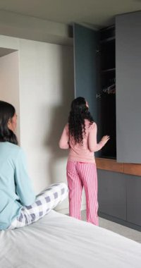 Dikey video: Tavsiye için yatak odasındaki dolaptan pantolon ve gömlek çıkaran bayan arkadaşları uyandırmak. Yatma, arkadaşlık, gündelik, modern, iç mekan, rahat, dikey video.