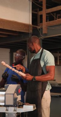 Dikey video: Afrika kökenli Amerikalı eğitmen çırakları eğitime uygun olarak çarkları ölçüyor. İşçilik, akıl hocalığı, ahşap işçiliği, eğitim, hassasiyet, takım çalışması, dikey video