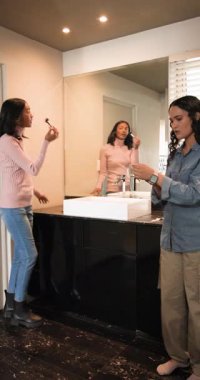 Dikey video: Makyaj fırçasını kaldıran Afrikalı Amerikalı arkadaşlar gösteriş hazırlığında küpe çeviriyorlar. Güzellik, arkadaşlık, kozmetik, mücevher, tımar, kadınlık, dikey video