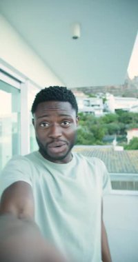 Dikey video: Çekici kamera, Afro-Amerikan adam tepe balkonunda izleyicileri selamlıyor. Modern, gündelik, açık hava, manzaralı, rahat, kendinden emin, dikey video