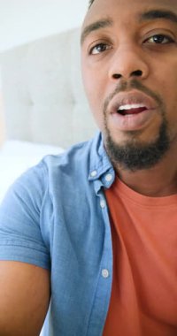 Dikey video: Kamera Afrikalı Amerikalı adamı tanıtıyor, yatak odasındaki cam kapıyı işaret ediyor. Portre, yaşam tarzı, konforlu, iletişim, ev içi, gündelik, dikey video