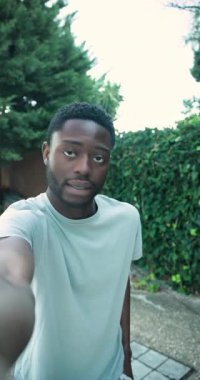 Dikey video: Afrikalı Amerikalı erkek kamera donanımını genişletiyor, arka bahçede video bloğu çekerken konuşuyor. İçerik oluşturucu, açık hava çekimi, günlük tarz, yaşam tarzı, kişisel marka, ev yapımı video, dikey video