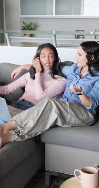 Dikey video: Kanepede dizüstü bilgisayarı gösteren çeşitli bayan arkadaşlar yazarken içeriğe tepki veriyorlar. İşbirliği, bağlantı, gündelik, modern, iletişim, arkadaşlık, dikey video