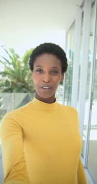 Dikey video: Balkonda konuşan akıllı telefonlu Afro-Amerikan kadın fitness bandını gösteriyor. Özgün, canlı, modern, yaşam tarzı, iletişim, sağlık, dikey video