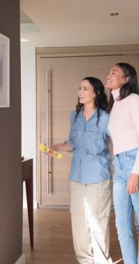 Dikey video: Koridora resim baskısı taşıyan kadın arkadaşlar, ruhsal seviyede baskı yapıyorlar. İşbirliği, takım çalışması, iç mekan, modern, yaratıcı, neşeli, dikey video