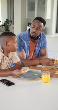 Dikey video: Afro-Amerikalı baba ve oğul fesleğene tepki gösterip gülüyorlar. Aile, eğlence, kırsal, samimi, sevecen, aşçı, dikey video