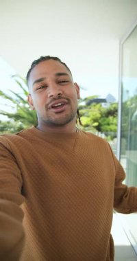 Dikey video: Balkon görünümlü terasta izleyicileri selamlayan akıllı telefon uzatan erkek sunucu. Açık hava, misafirperverlik, yaşam tarzı, kentsel, doğal, iletişim, dikey video