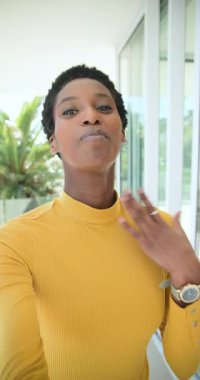 Dikey video: Sarı üst sallanan ve balkonda saatini gösteren Afro-Amerikan kadın kaydı. Portre, yaşam tarzı, canlı, açık hava, iletişim, özgünlük, dikey video