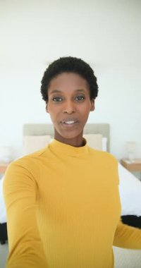 Dikey video: Elinde telefonla yatak odasına giren Afro-Amerikan kadın el sallıyor ve yatak turu yapıyor. Yaşam tarzı, sağlık, modern, ev, iç mekan, iletişim, dikey video