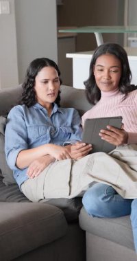 Dikey video: Değişen tableti inceleyen, kanepede işaret eden ve tartışan çeşitli bayan arkadaşlar. İşbirliği, arkadaşlık, teknoloji, rahatlama, modern, gündelik, dikey video