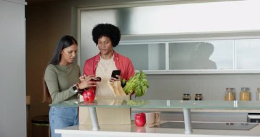 Mutfak adasındaki çantadan kırmızı biber ve zeytinyağı çıkaran çeşitli çiftler yemek tariflerini kontrol ederken. Aile içi, işbirliği, enerjik, sağlıklı, yemek pişirme, modern, konukseverlik.