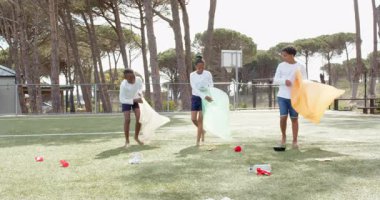 Çocuk parkını temizlemek, çok ırklı öğrenciler renkli çantalarla çöp toplamak. Topluluk, gönüllü, temizlik, çevre, takım çalışması, açık hava