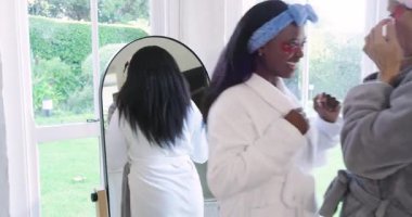 Farklı bayan arkadaşlar aynanın karşısına geçip yamaları düzeltiyor, krema sürüyor ve çay içiyorlar. Rahatlama, dostluk, cilt bakımı, spa, sağlık, rahatlık, aydınlık