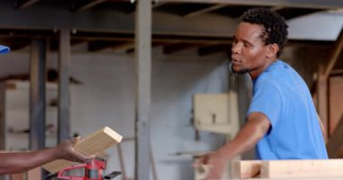 Marangozluk atölyesinde çalışan Afrika kökenli Amerikalı iş arkadaşlarını elektrikli matkapla kontrol ediyorlar. İşçilik, takım çalışması, endüstriyel, ahşap işçiliği, inşaat, işbirliği, nitelikli işçilik