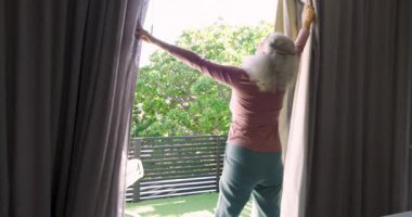 Üst düzey bir çift, sabah güneşinin içeri girmesine ve kahve fincanlarından yudumlamasına izin vermek için balkonda perdeler açıyor. Romantik, rahat, sakin, açık hava, yaşam tarzı, huzurlu, ev