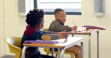 Okulda, iki çok ırklı çocuk sınıf masasında ödevlerini yapıyor, fikirlerini paylaşıyorlar. İşbirliği, takım çalışması, eğitim, okula dönüş, öğrenme, öğrenim