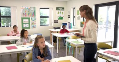 Öğretmen tableti tutarken öğrenciler hevesle sınıfta el kaldırıyorlar. Eğitim, öğrenme, öğretim, teknoloji, müdahale, etkileşim