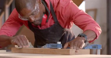 Afrika kökenli Amerikalı bir adamı zımpara kağıdına basarak tezgahta güvenlik gözlükleriyle zımparalıyor. Sanatçılık, marangozluk, zanaatkarlık, el işi, endüstriyel, makine, hassasiyet