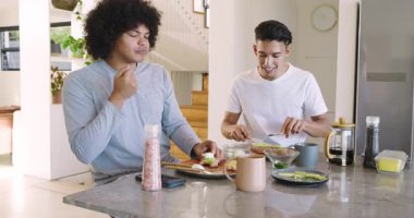 Avokado kepçelemek, mermer adada karabiber değirmeni kullanan erkek arkadaşlar, kahvaltıda kupa paylaşmak. Aşçılık, arkadaşlık, gündelik, modern, yaşam tarzı, sağlık, akşam yemeği