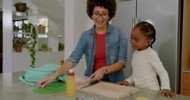 Anne ve kızı havuç paketleyip beslenme çantasına koyuyorlar. Okul için mutfak adasında sırt çantası veriyorlar. Aile, bakım, beslenme, organizasyonel, yaşam tarzı, renk paleti, iç mekan