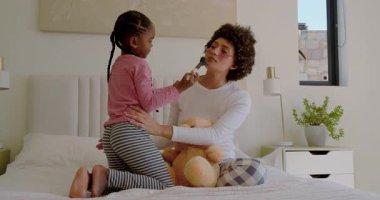 Afrika kökenli Amerikalı anne ve kız fırça kullanıyor, oyuncak ayıyla yatak muhabbeti yapıyorlar. Aile, bakım, şefkat, konforlu, oyuncu, yaşam tarzı, şefkat