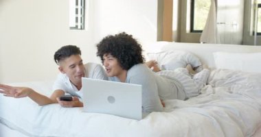 Telefon uyarısı. Yataktaki farklı erkek çifti telefona bakmaya, gülmeye ve dizüstü bilgisayarın yanında sarılmaya çağırıyor. Romantizm, samimiyet, rahatlama, modern, rahat, bağlantı, boş zaman