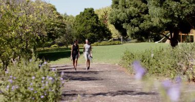 Çeşitli bayan arkadaşlar parkta yürürken ve su şişeleriyle konuşurken ağacı işaret ediyorlar. Açık hava, arkadaşlık, aktivite, eğlence, refah, coşku, eğlence.