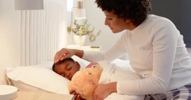 Afrika kökenli Amerikalı anne yatak odasında göğsüne oyuncak ayı koyuyor, çocuğunu sakinleştiriyor. Şefkat, rahatlık, aile, beslenme, huzur, uyku zamanı, rahatlık