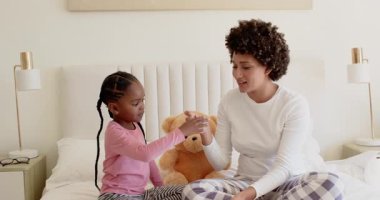 Afrika kökenli Amerikalı anne, pudra kutusunu açıyor ve kızına bağlanmak için yatağa allık sürüyor. Annelik, bağlılık, beslenme, yakınlık, aile, bakım, şefkat.