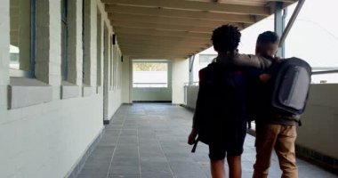 Okulda sırt çantaları taşıyan çok ırklı çocuklar koridorda kol kola yürüyorlar. Arkadaşlık, çok ırklı çocuklar, birliktelik, eğitim