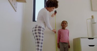 Büyümenin etkisiyle, anne ve kızı sarı şeritli ölçü, yatak odasının yüksekliğini gösteriyor. Aile, bağ, ölçüm, büyüme, yetiştirme, çocukluk, ev