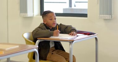 Okulda, masadaki deftere yazı yazan genç bir çocuk, işine konsantre oluyor. Eğitim, eğitim, konsantrasyon, öğrenim, çocukluk, akademik