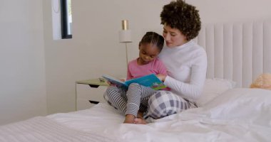 Afrika kökenli Amerikalı anne ve kız, bağlanmak için resimde yatakta kıkırdamalar üzerine kitap okuyor. Ebeveynlik, okur-yazarlık, rahat, terbiye, eğitim, bağlanma, aile