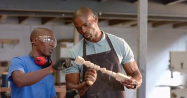 Afro-Amerikan iş arkadaşlarını incelerken tezgah tezgahında kırmızı kulaklıklar takıyorlar, Milli ve talaş ile. El işi, takım çalışması, endüstriyel, kırsal, öğrenme, işbirliği, atölye