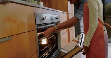 Çeşitli anne ve kızlar mutfağa girip kek tepsisi tutarak dans etmek için fırına koyuyorlar. Aile, bağ, kutlama, aile içi, eğlence, yaşam tarzı, konforlu