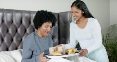 Afro-Amerikalı bir adam yemek için Hintli bir kadından kahvaltı tepsisi alıyor ve gülüyor. Romantik, samimiyet, sabah, sevgi, konfor, arkadaşlık, yaşam tarzı