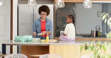 Afro-Amerikan anne mutfakta havuç doğruyor, sırt çantasında atıştırmalık paketliyor, kızına sarılıyor. Yurt içi, yetiştirme, yaşam tarzı, çağdaş, bakıcı, ailevi, neşeli