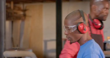 Afrika kökenli Amerikalı bir adam, eldiven giyip atölyedeki tahta testereye itme engeli takmıştı. Ahşap işçiliği, işçiliği, inşaat, sanayi, el emeği, araç kullanımı, çalışma alanı